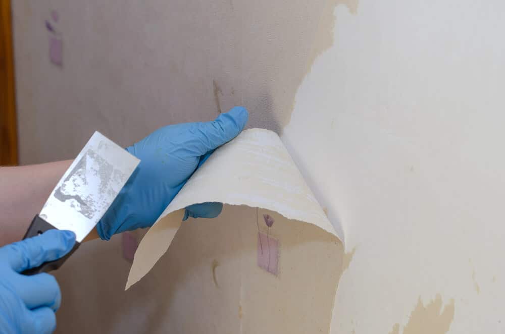 A-woman-wearing-blue-gloves-is-removing-old-wallpaper